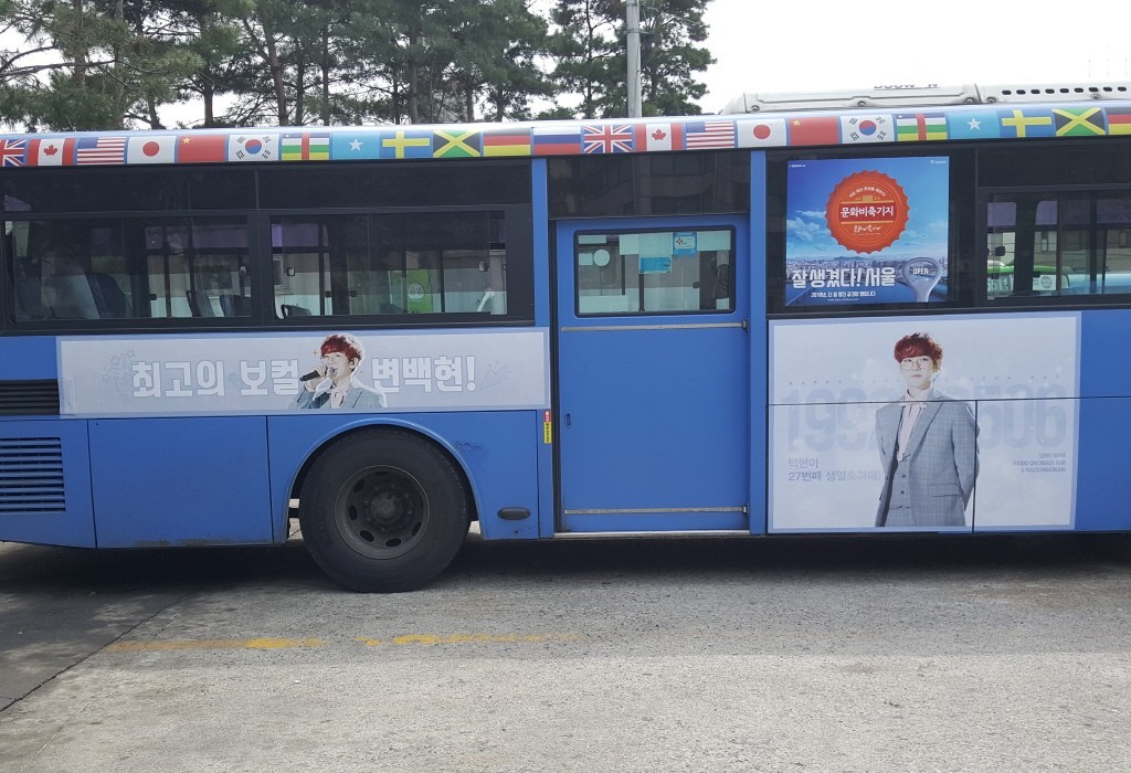 Door side of the bus with a pale banner of Korean text and a larger section showing a photo and a Korean greeting for a 27th birthday