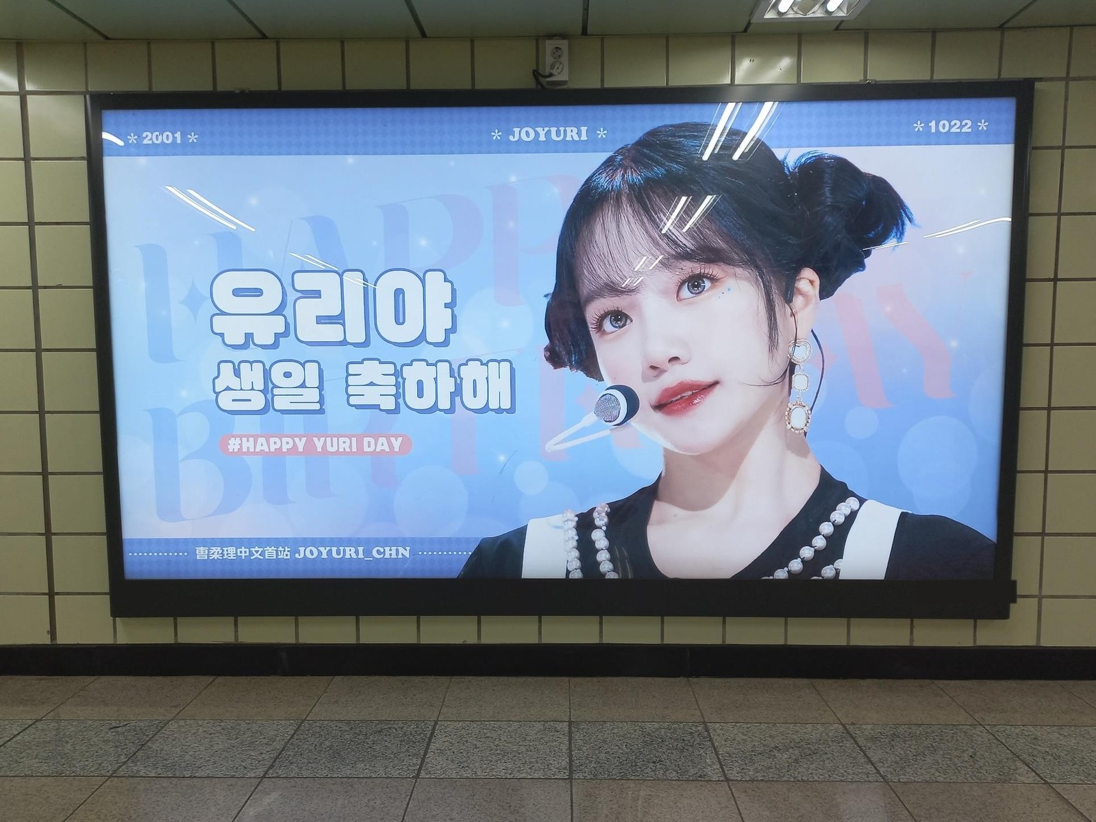 Jo Yuri birthday ad in a lit subway lightbox on a tiled station wall, with a large Korean birthday greeting on a pale blue background