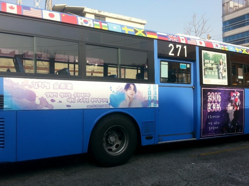 Heechul debut anniversary ad on the side of a blue Seoul city bus, with a watercolour-style banner and a dark purple panel showing the numbers 2005 0306