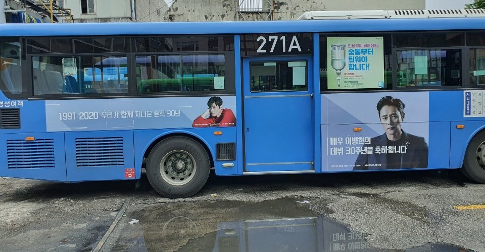 Door side of the same bus with a narrow banner showing 1991-2020 and a taller panel with a portrait next to the door