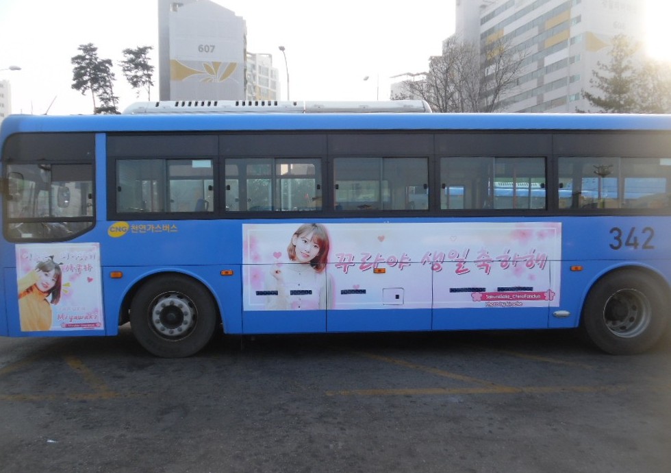 Miyawaki Sakura birthday ad on the road side of a blue Seoul city bus, a pale pink panel with her photo and a Korean birthday greeting