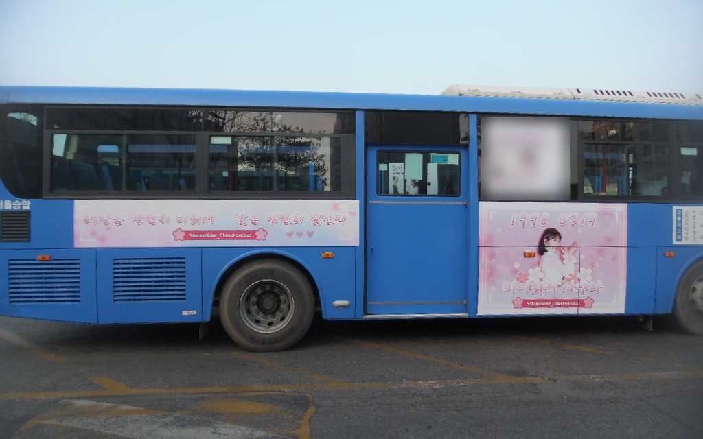 Door side of the bus with a long pink banner of Korean handwriting-style text and a square panel showing the date 1998 0319