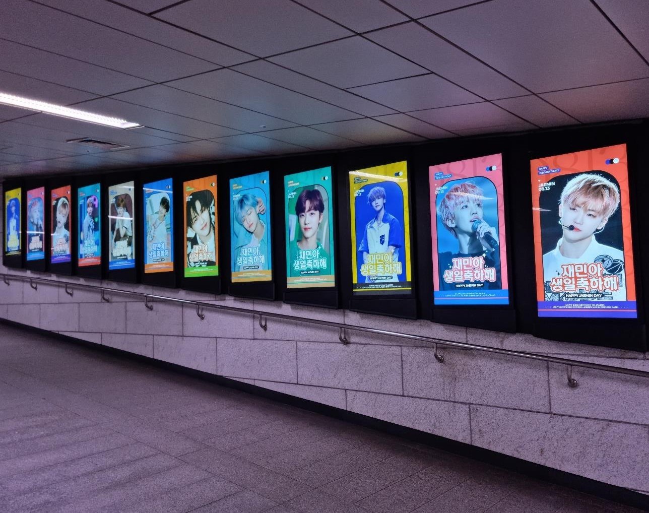 A row of twelve upright digital screens along a station passage, each showing a different Jaemin birthday design