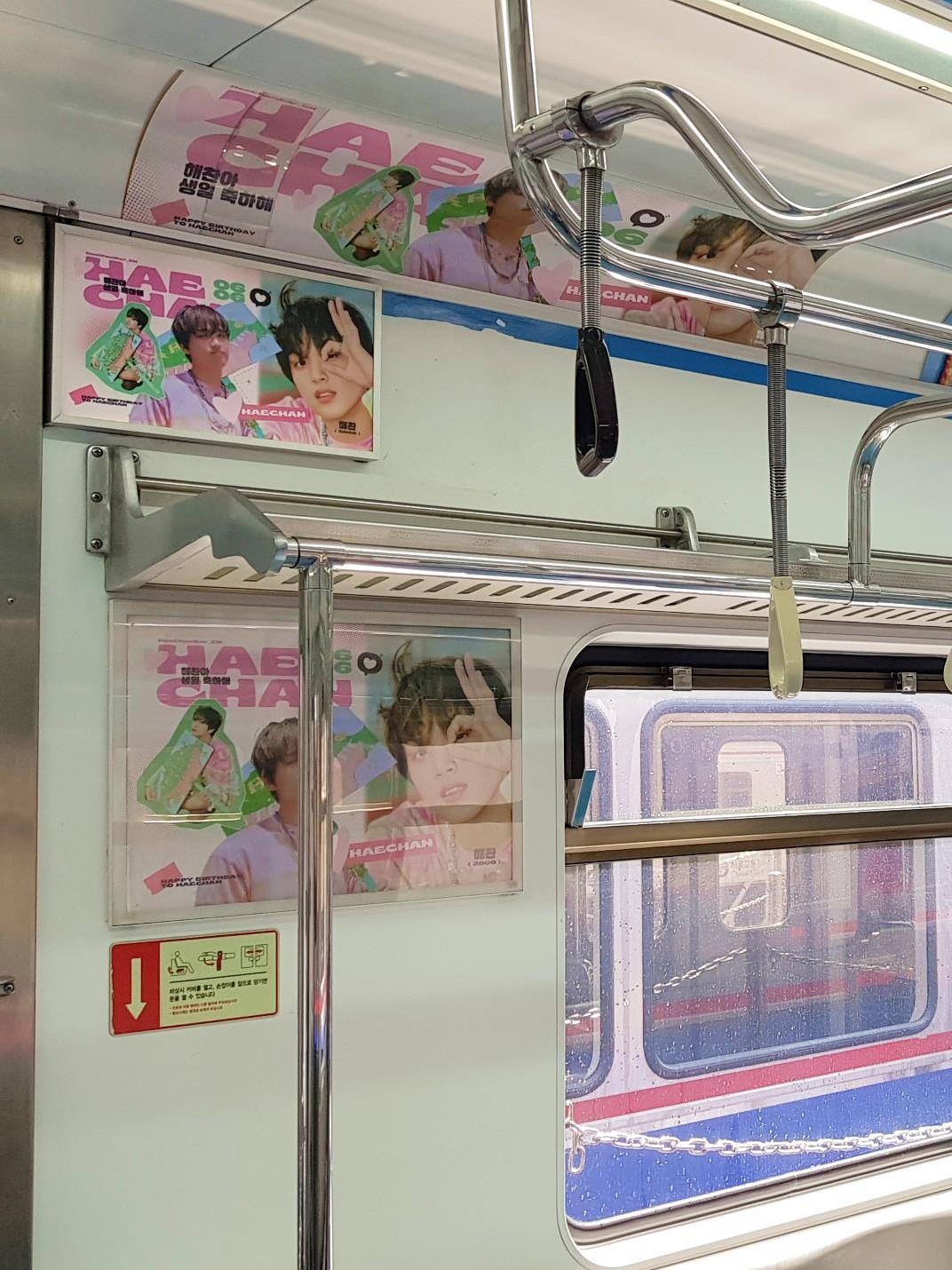 Posters beside a train window and on the curved panel above the luggage rack