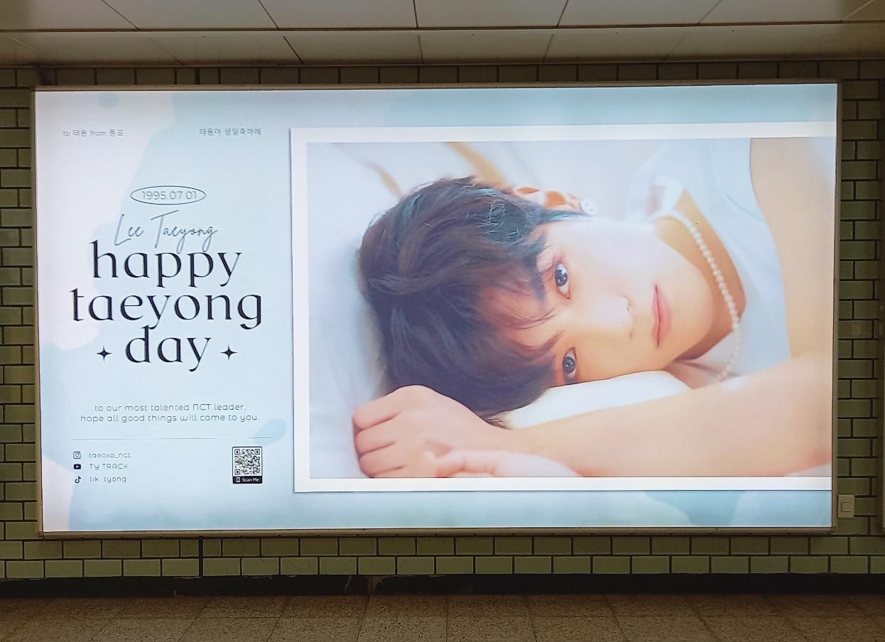 Taeyong birthday ad in a subway lightbox on a green tiled wall, with "happy taeyong day" on the left and a large photo on the right