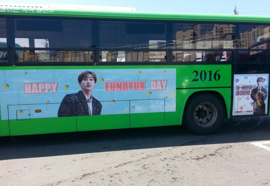Eunhyuk birthday ad on the side of a green Seoul city bus, a light blue banner reading Happy Eunhyuk Day with a photo in the middle